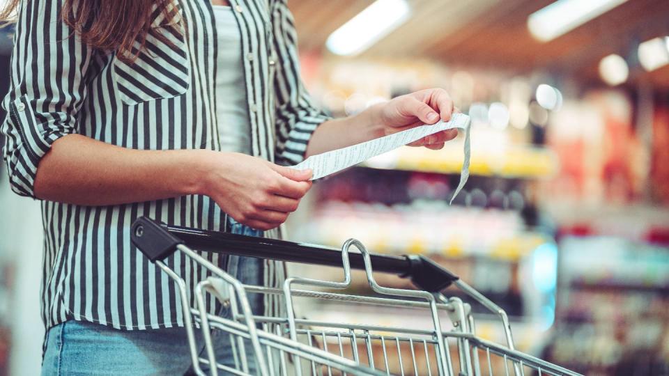 Femme devant un caddie lisant un ticket de caisse