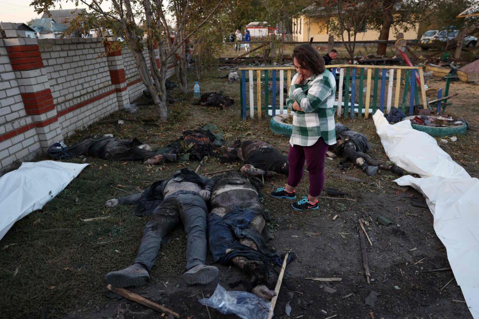 A woman stands next to bodies being carried out of a destroyed shop and cafe after a Russian strike in the village of Groza in Ukraine on Oct. 5, 2023.