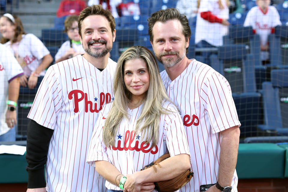 Will Friedle, Danielle Fishel, and Rider Strong pose together at a stadium wearing Philadelphia Phillies jerseys