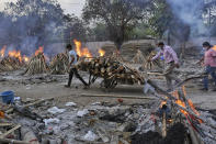 A worker carries wood on a hand cart as multiple funeral pyres of COVID-19 victims burn at a crematorium on the outskirts of New Delhi, India, Saturday, May 1, 2021. India on Saturday set yet another daily global record with 401,993 new cases, taking its tally to more than 19.1 million. Another 3,523 people died in the past 24 hours, raising the overall fatalities to 211,853, according to the Health Ministry. Experts believe both figures are an undercount. (AP Photo/Ishant Chauhan)