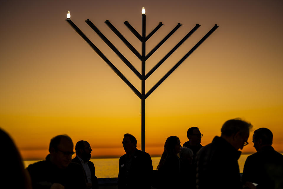 FILE - People gather around the 10-foot menorah during the "Hanukkah on the Pier" event at the end of the San Clemente pier hosted by Chabad of San Clemente in San Clemente, Calif., Sunday, Dec. 18, 2022. On eight consecutive nightfalls, Jews gather with family and friends to light one additional candle in the menorah candelabra. They do so to commemorate the rededication of the Temple in Jerusalem in the 2nd century BC, after a small group of Jewish fighters liberated it from occupying foreign forces. (Leonard Ortiz/The Orange County Register via AP, File)