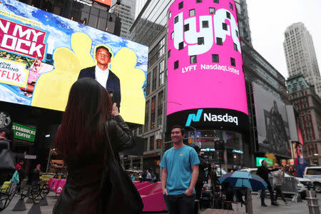 Brian Friedenberg, an intern for Lyft, has his picture taken in front of signage for Lyft as it is displayed at the NASDAQ MarketSite in Times Square in celebration of its initial public offering (IPO) on the NASDAQ Stock Market in New York, U.S., March 29, 2019. REUTERS/Shannon Stapleton/File Photo