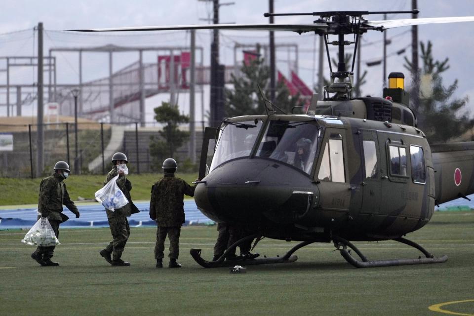 Members of the Japan Ground Self-Defense Force carry bottled water to a helicopter before taking off from a temporary landing site in Wajima in the Noto peninsula, facing the Sea of Japan, northwest of Tokyo, Saturday, Jan. 6, 2024, following Monday's deadly earthquake. (AP Photo/Hiro Komae)