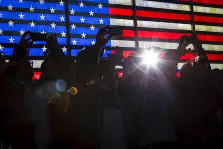 A flash goes off as people stand in front of and take pictures of a billboard by Revlon that takes their pictures and displays them on the billboard in Times Square in the Manhattan borough of New York October 13, 2015. REUTERS/Carlo Allegri