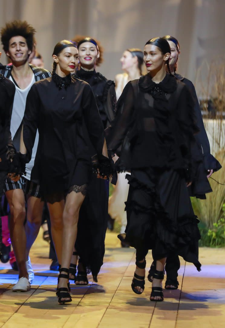 Gigi Hadid (L) and her sister Bella Hadid (R) give each other knowing glances as they walk the runway while Bella's ex-boyfriend, The Weeknd, performs during the H&M Studio show in Paris, France. (Photo: Splash News)