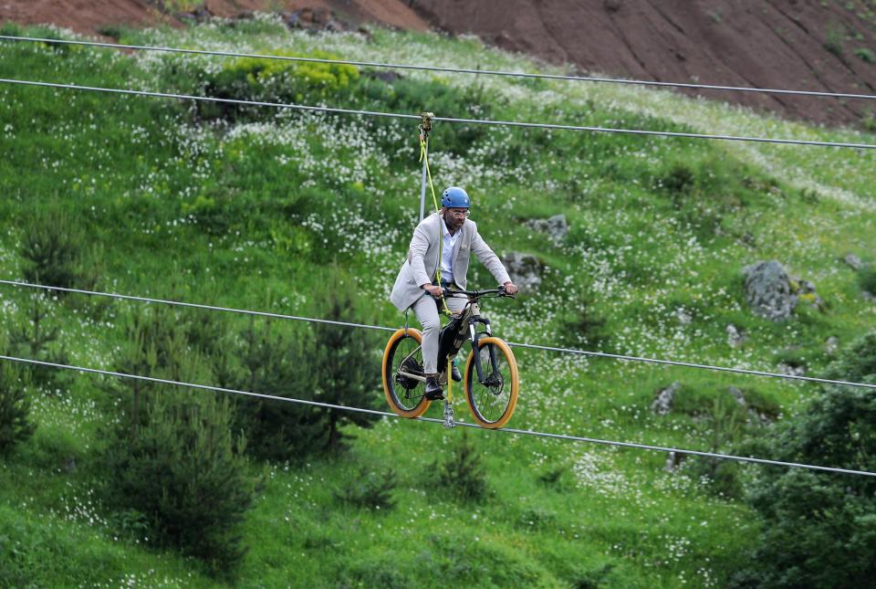 a man rides a bike on a zip line during the opening ceremony of a glass bar and glass bridge over Dashbashi Canyon