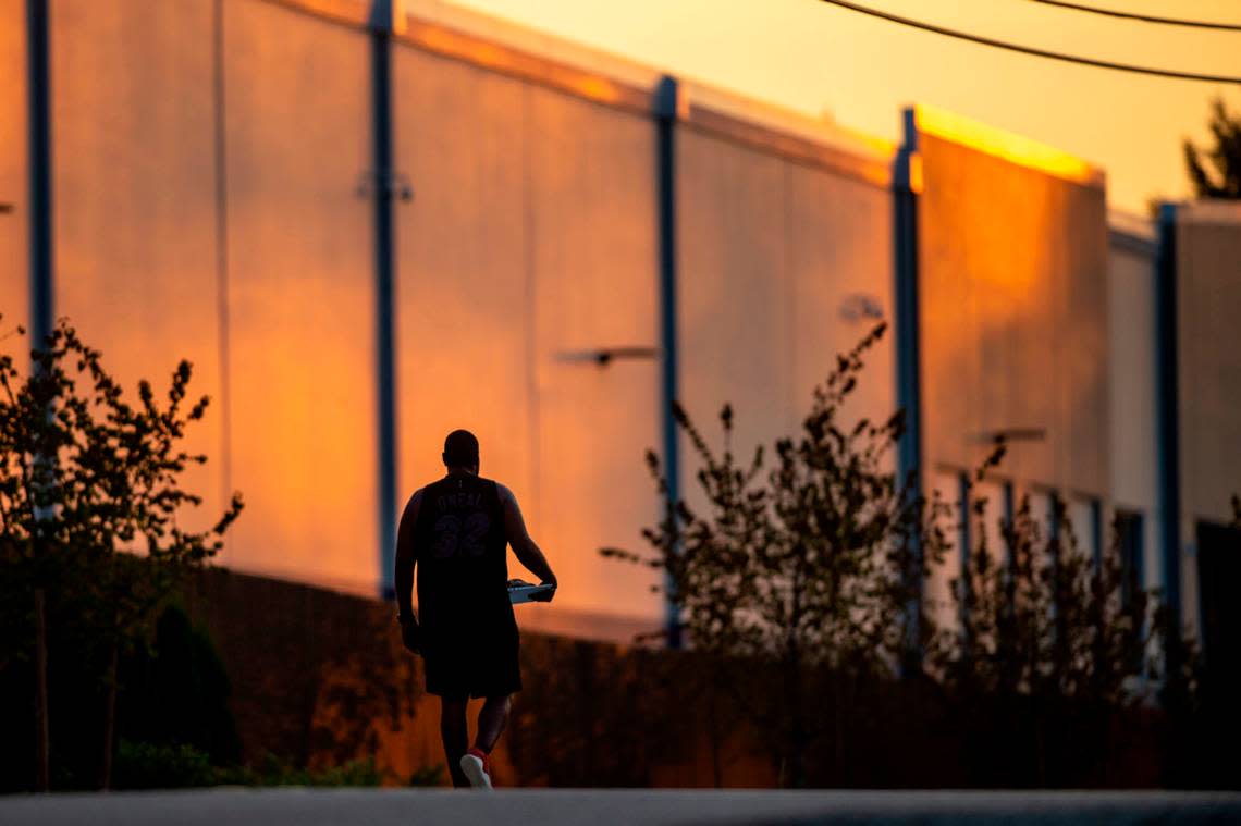 A man walks along 146th Street Southwest past a large Amazon warehouse as the sun sets in Lakewood, Wash., on Thursday, Aug. 18, 2022.