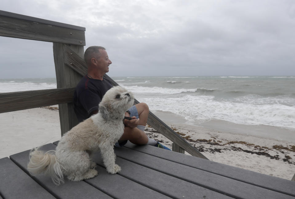 Kent Ahern and his dog Blanco watch waves churned up by Tropical Storm Isaias near Jaycee Beach Park, Sunday, Aug. 2, 2020, in Vero Beach, Fla. Isaias weakened from a hurricane to a tropical storm late Saturday afternoon, but was still expected to bring heavy rain and flooding as it barrels toward Florida. (AP Photo/Wilfredo Lee)