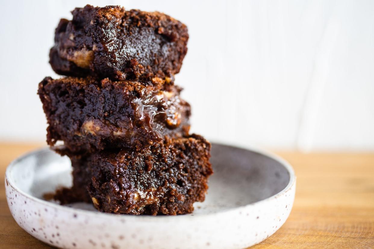 Pile of moisty chocolate brownie on a white ceramic and wood table.