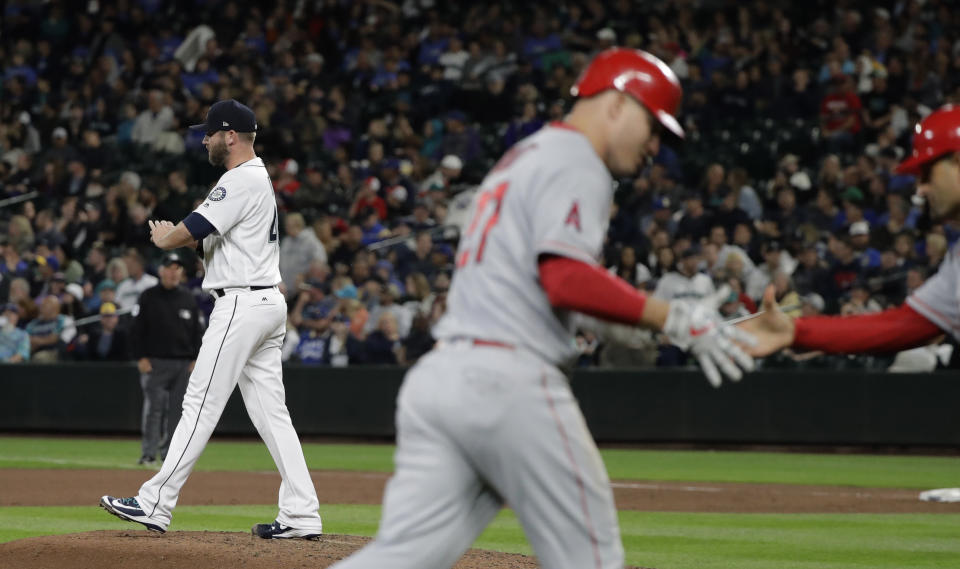 Seattle Mariners pitcher Ryan Cook, left, stands on the mound as the Angels’ Mike Trout greets third-base coach Dino Ebel after Trout hit a two-run home run. (AP)