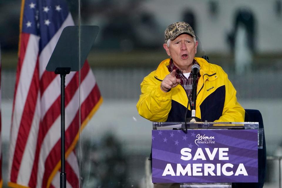 Mo Brooks speaks in front of an american flag and behind a podium that says save america