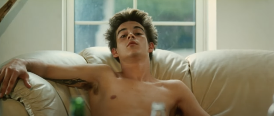 A teenager sits shirtless on his couch