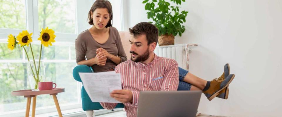 Beautiful young couple managing their finances, reviewing bank accounts on laptop computer, calculating bank loans and debts and making payments online