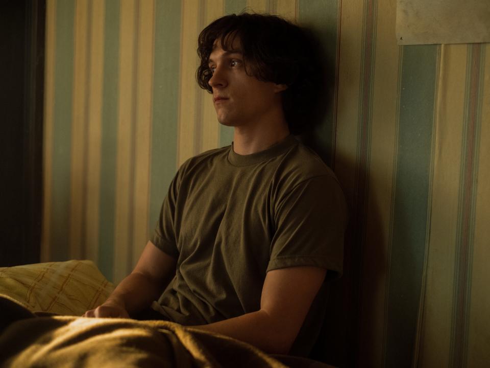 Tom Holland wearing a green shirt with his back against a wall with blue-and-yellow-striped wallpaper on "The Crowded Room."