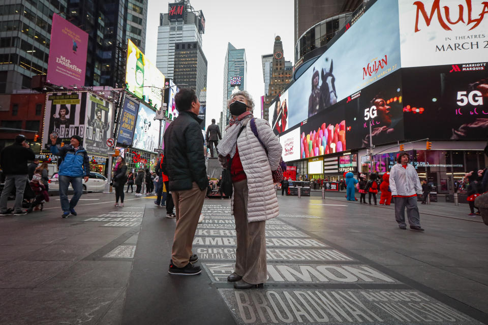 A pedestrian wearing a face mask stops in Times Square, Thursday, March 12, 2020, in New York. New York City Mayor Bill de Blasio said Thursday he will announce new restrictions on gatherings to halt the spread of the new coronavirus in the coming days. For most people, the new coronavirus causes only mild or moderate symptoms. For some it can cause more severe illness. (AP Photo/John Minchillo)