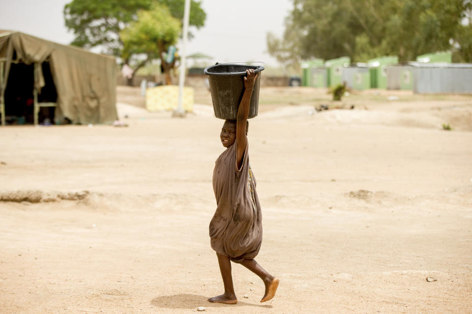 FILE - A child passes by carrying a bucket in Yola, Nigeria, April 22, 2016. Droughts, flooding and a shrinking Lake Chad caused in part by climate change is fueling conflict and migration in the region and needs to better addressed, a report said Thursday, Jan. 19, 2023. (AP Photo/Andrew Harnik, File)