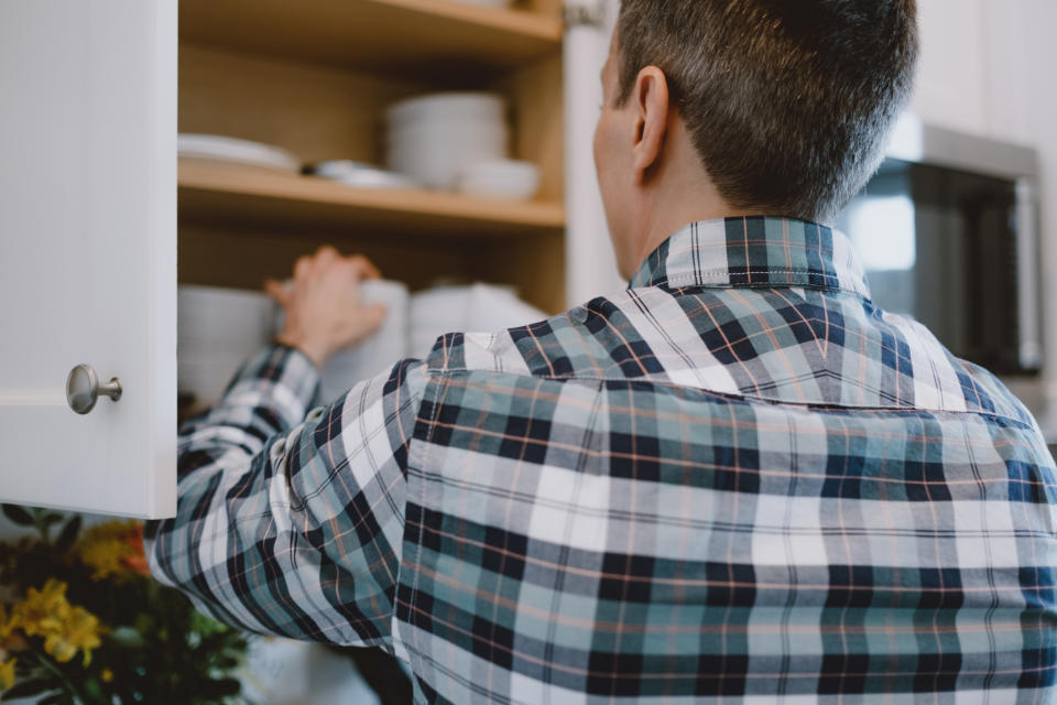 Person in a plaid shirt reaching for an item in a kitchen cabinet