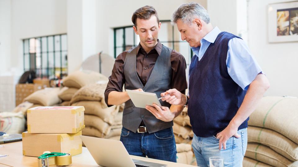 Two business men working at coffee storage room and looking at digital tablet.