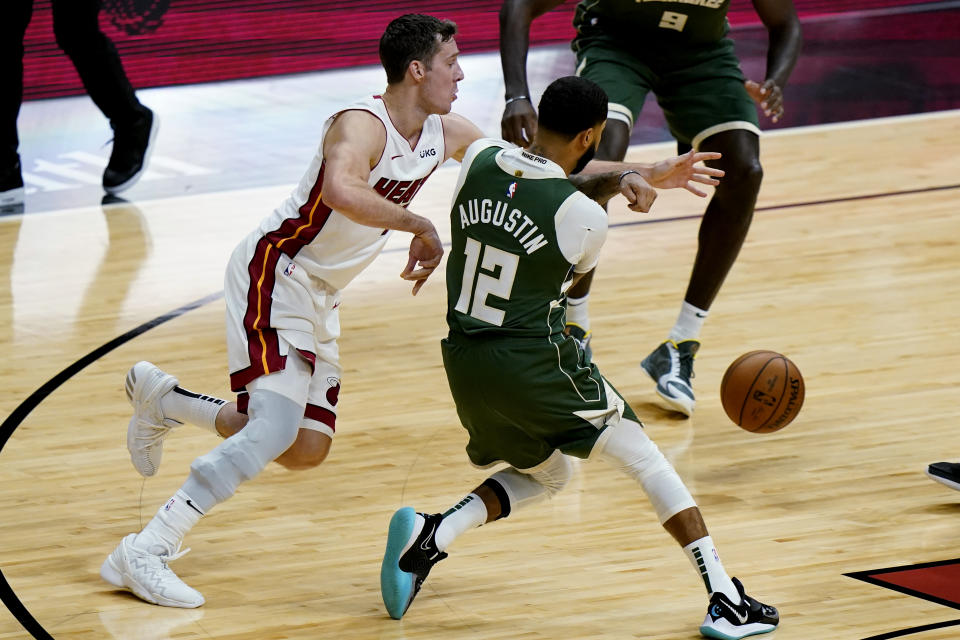 Miami Heat guard Goran Dragic, left, passes the ball as Milwaukee Bucks guard D.J. Augustin (12) defends defends during the first half of an NBA basketball game, Wednesday, Dec. 30, 2020, in Miami. (AP Photo/Lynne Sladky)