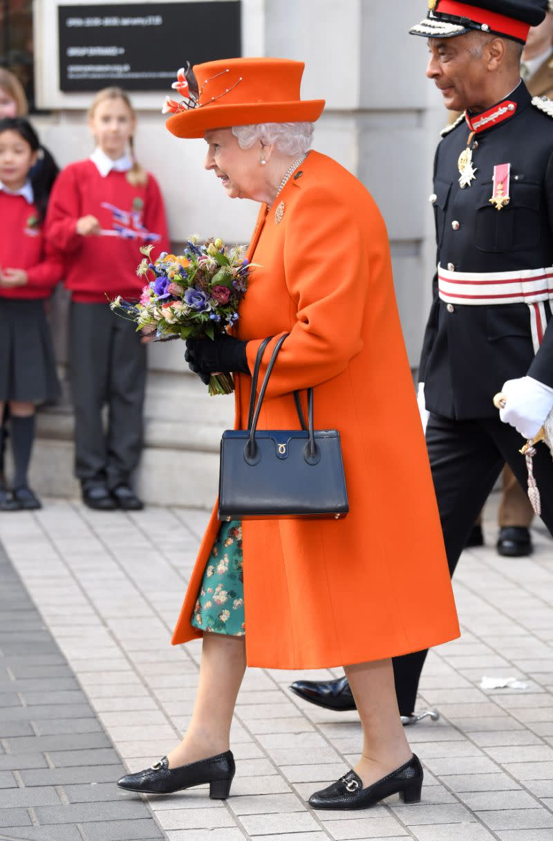 Queen Elizabeth trägt eine schwarze Launer-Handtasche und einen leuchtend orangefarbenen Mantel. (Getty Images)