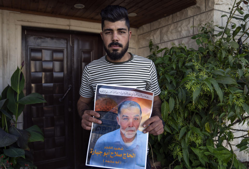 Mohammad, 26, son of Palestinian Salah Sawafta who was shot and killed during an Israeli army arrest raid in the occupied West Bank on Aug. 19, 2022, poses with a poster with his father's name and picture and Arabic that reads, "the dawn's Martyr," in the West Bank city of Tubas, Thursday, Aug. 25, 2022. At least 85 Palestinians have been killed in the West Bank this year as Israeli forces have carried out nightly raids in cities, towns and villages, making it the deadliest in the occupied territory since 2016. (AP Photo/Nasser Nasser)