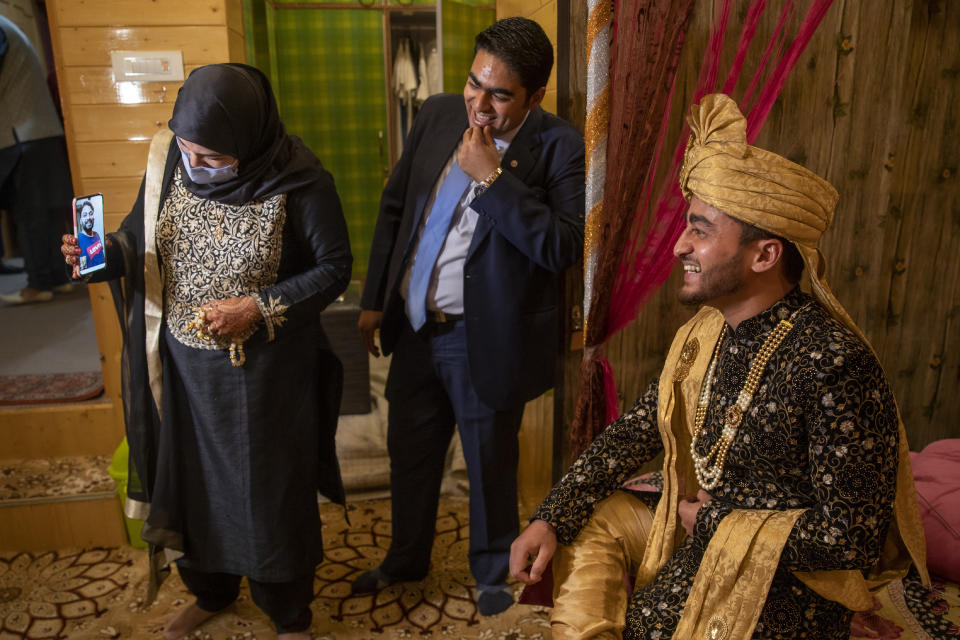 Khusheeba Munir, holds the cell phone as her husband Azhar Mahmood, who tested positive for COVID-19 and was not able to attend the marriage shares a lighter moment with his cousin and groom Haseeb Mushtaq, during a wedding ceremony on the outskirts of Srinagar, Indian controlled Kashmir, Monday, Sept. 14, 2020. The coronavirus pandemic has changed the way people celebrate weddings in Kashmir. The traditional week-long feasting , elaborate rituals and huge gatherings have given way to muted ceremonies with a limited number of close relatives attending. With restrictions in place and many weddings cancelled, the traditional wedding chefs have little or no work. The virus has drastically impacted the life and businesses in the region. (AP Photo/ Dar Yasin)