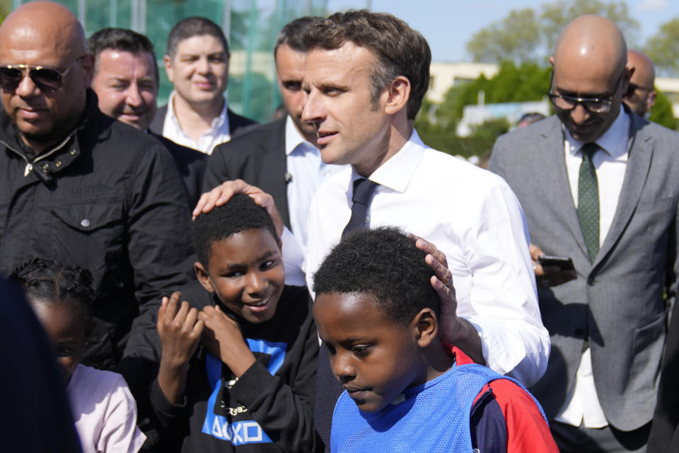 Centrist presidential candidate and French President Emmanuel Macron greets youths as he campaigns in the Auguste Delaune stadium Thursday, April 21, 2022 in Saint-Denis, outside Paris. French voters head to polls on Sunday in a runoff vote between centrist incumbent Emmanuel Macron and nationalist rival Marine Le Pen. (AP Photo/Francois Mori, Pool)