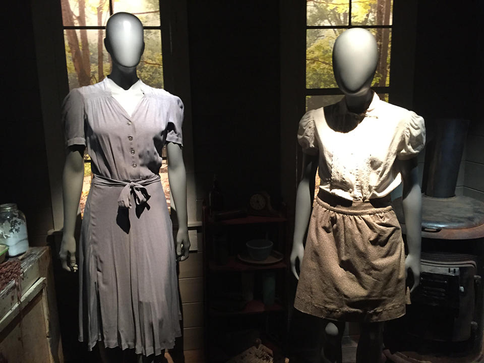 Here are the very modest dresses worn by Katniss and Prim in the early part of the first Hunger Games film, back at home in District 12. The props from the house that you see in the background — like the stove and shelving unit —are straight from the set.