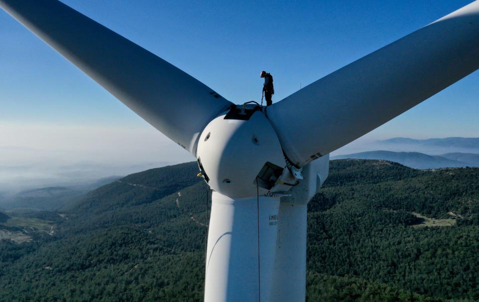 A rope access technicians stands on top of a wind turbine