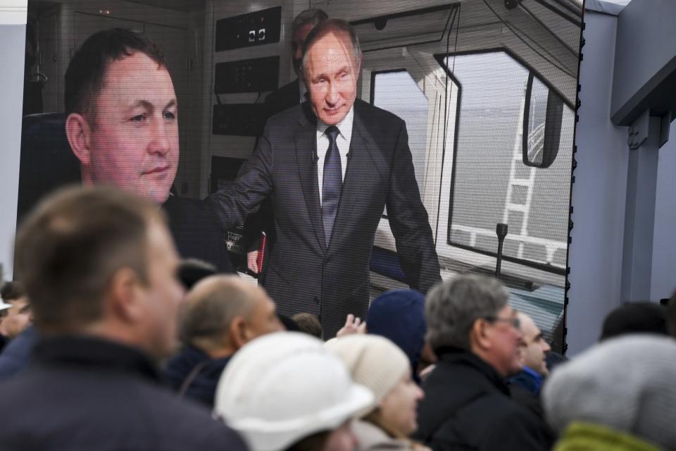 People watch a giant TV screen with Russian President Vladimir Putin riding a train across a bridge linking Russia and the Crimean peninsula in Taman, Russia, Monday, Dec. 23, 2019. Putin on Monday inaugurated a railway bridge to Crimea, the longest in Europe, which is intended to facilitate links with Crimea, which Russia annexed from Ukraine in 2014. (AP Photo)