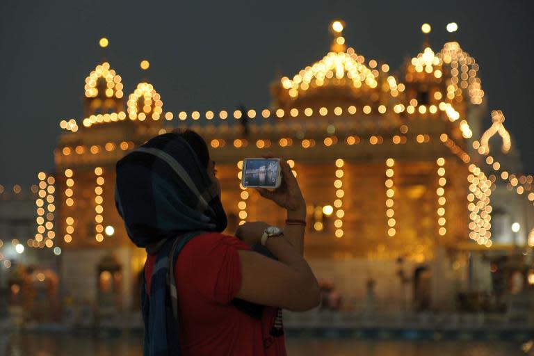 An Indian Sikh devotee takes a photograph on her mobile phone in the front of the illuminated Sikhism's holiest shrine, the Golden Temple in Amritsar on the April 18,2014