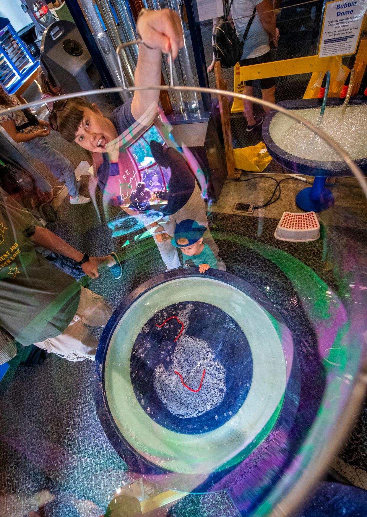 Fontaine Landgrebe makes a large bubble as her son Titus Landgrebe watches during BubbleFest at WonderLab Science Museum on Saturday, June 17, 2023.