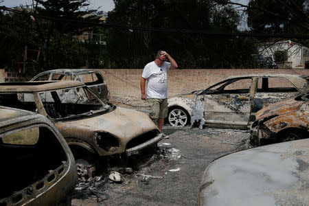 A local reacts as he stands next to burnt cars following a wildfire at the village of Mati, near Athens, Greece, July 24, 2018. REUTERS/Costas Baltas