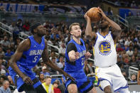 Golden State Warriors forward Andrew Wiggins, right, looks for a shot against Orlando Magic forward Franz Wagner, center, and center Mo Bamba (5) during the first half of an NBA basketball game, Tuesday, March 22, 2022, in Orlando, Fla. (AP Photo/John Raoux)