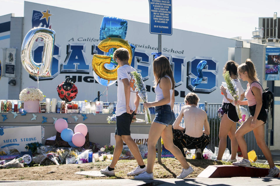 High school students bring flowers to a memorial, Monday, Nov. 18, 2019, for two students killed during a shooting at Saugus High School in Santa Clarita, Calif., several days earlier. The students will return to school on Dec. 2. (Sarah Reingewirtz/The Orange County Register via AP)