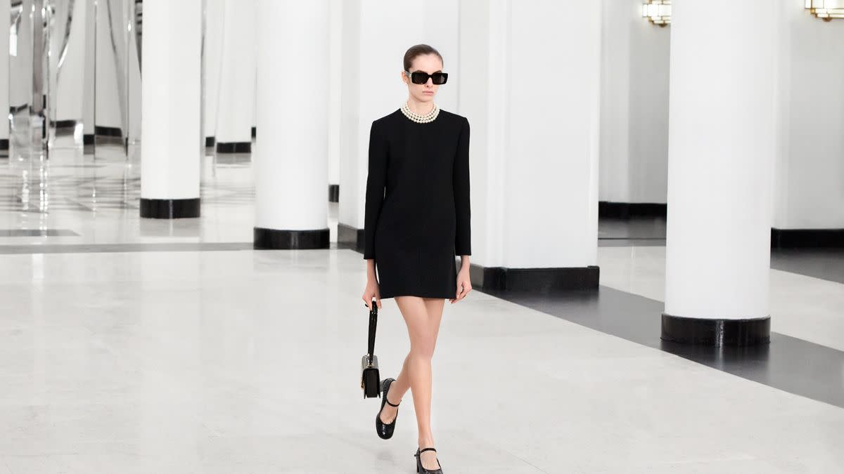 a man wearing a black dress and sunglasses walking in a large room