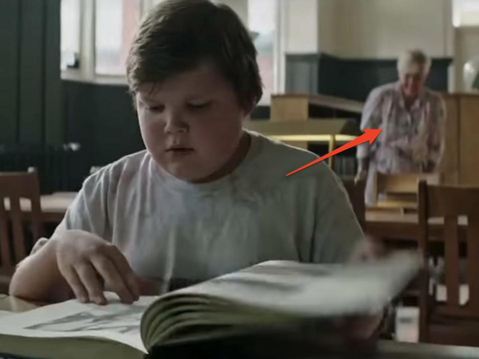 a boy reading at a library with an older woman blurred out in the background in "It."