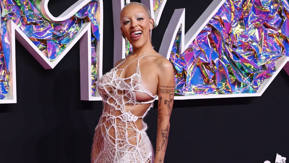 Doja Cat wore a daring Ap0cene gown paired with see-through pointed pumps, diamond chandelier earrings and glittery wraparound silver bracelets. Her makeup continued the theme with spidery black eyelashes and a bold white eyeshadow and thin arched brows.  - Gilbert Flores/Variety/Getty Images