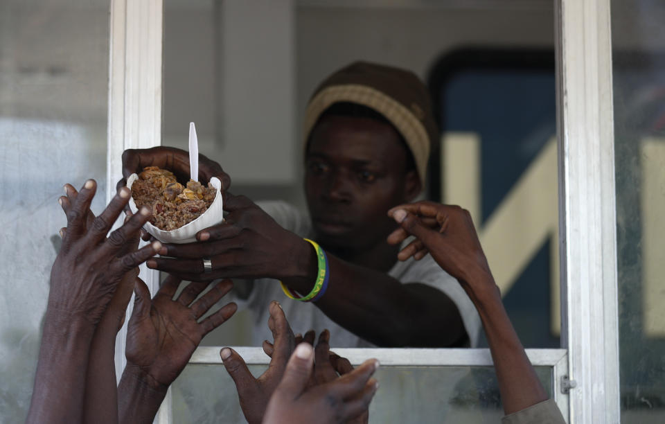 A man hands out a meal of beans and rice, during a federal government distribution of food and school supplies to some residents of Cite Soleil, in Port-au-Prince, Haiti, Thursday, Oct. 3, 2019. The daily struggles of Haitians have only become more acute as recent anti-government protests and roadblocks force the closure of businesses, sometimes permanently, as people lose jobs and dwindling incomes fall behind a spike in prices. (AP Photo/Rebecca Blackwell)