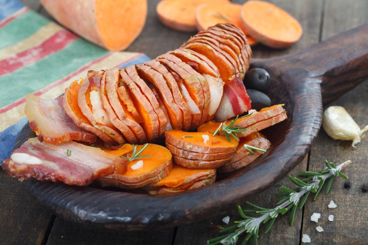 hasselback sweet potato with garlic and olives, salt, in wooden spoon
