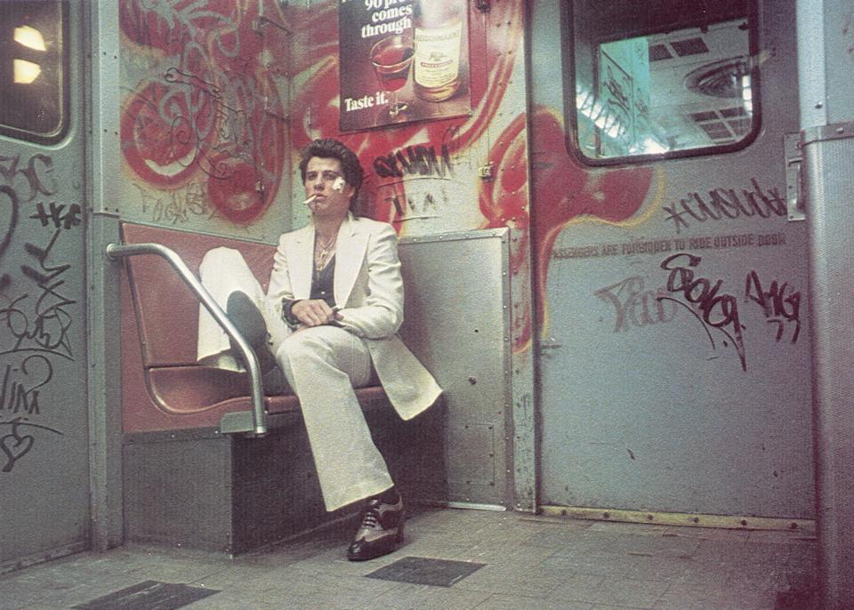 1977, American actor John Travolta sits on a bench inside a subway car painted with graffiti in a still from director John Badham's film 'Saturday Night Fever'. (Photo by Paramount Pictures/Getty Images)