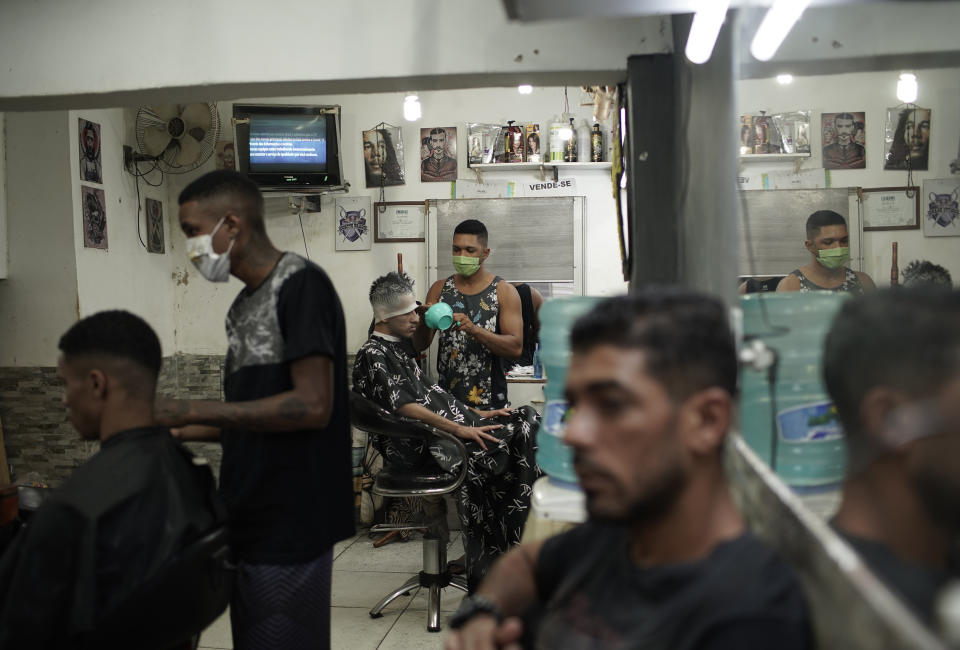 Haircutters, wearing protective face masks as a precaution against the new coronavirus, attend clients in a barbershop in the Mandela slum of Rio de Janeiro, Brazil, Tuesday, April 21, 2020. (AP Photo/Silvia Izquierdo)
