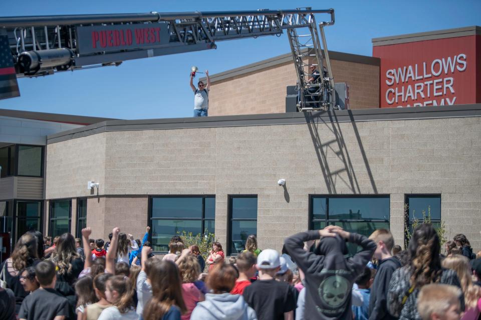 Swallows Charter Academy Principal Matthew Hawken waves to students from the top of the school. Hawken was lifted to the roof of the school by the Pueblo West Fire Department where he stayed overnight to celebrate a student reading challenge on Wednesday, April 24, 2024.