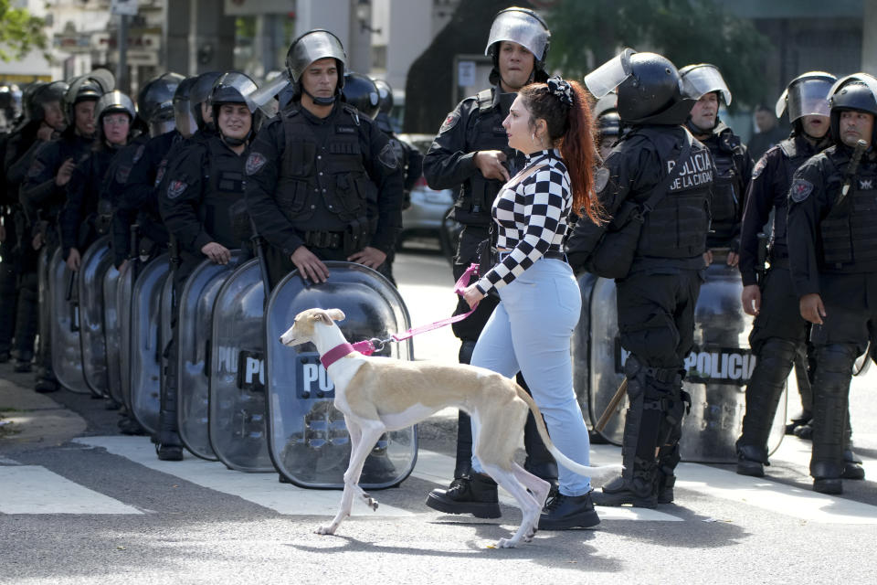 A woman walks her dog past police after they dispersed an anti-government protest against food scarcity at soup kitchens and against economic reforms proposed by President Javier Milei in Buenos Aires, Argentina, Wednesday, April 10, 2024. (AP Photo/Natacha Pisarenko)