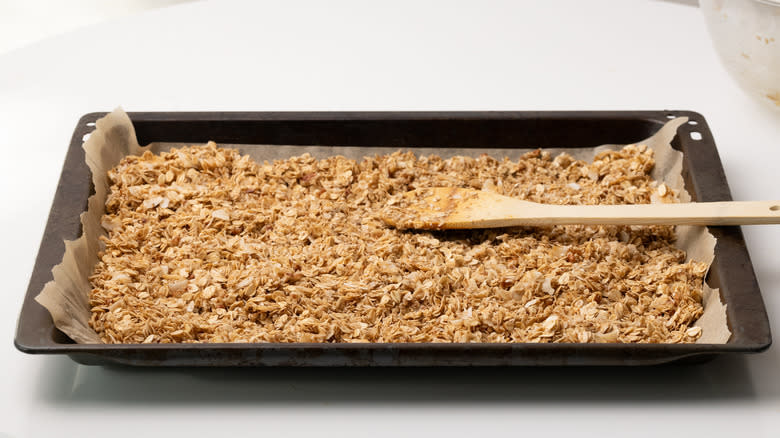 granola on a baking tray with wooden spoon