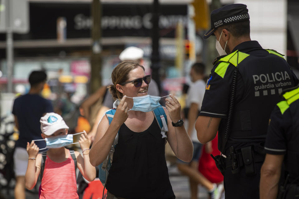 Catalonian police officers ask at a woman to wear a face mask, in Las Ramblas of Barcelona, Spain, Thursday, July 9, 2020. Authorities in northeast Spain will start fining individuals who do not wear face masks 100 euros ($113) as of Thursday when their use becomes obligatory in Barcelona and the surrounding Catalonia region. (AP Photo/Emilio Morenatti)