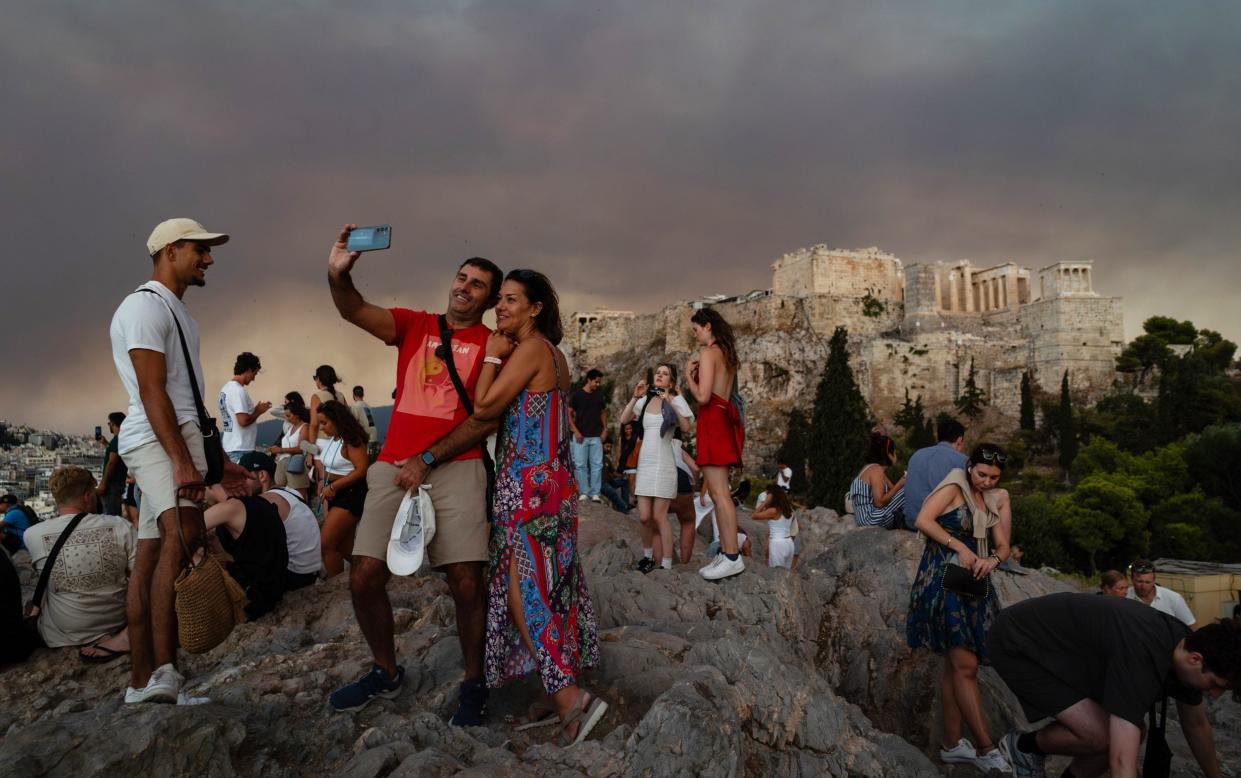 Tourists take selfie photos with the Acropolis citadel in the background as smoke from wildfires fills the sky above Athens