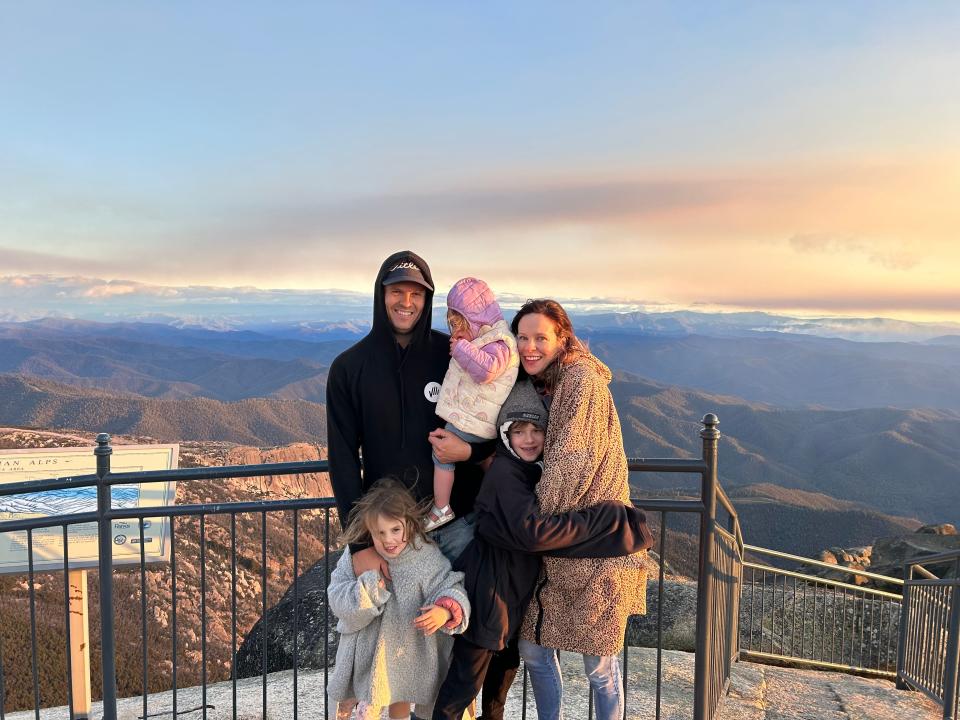 Melissa Noble with her husband and three kids standing on top of a mountain with a view in the background.