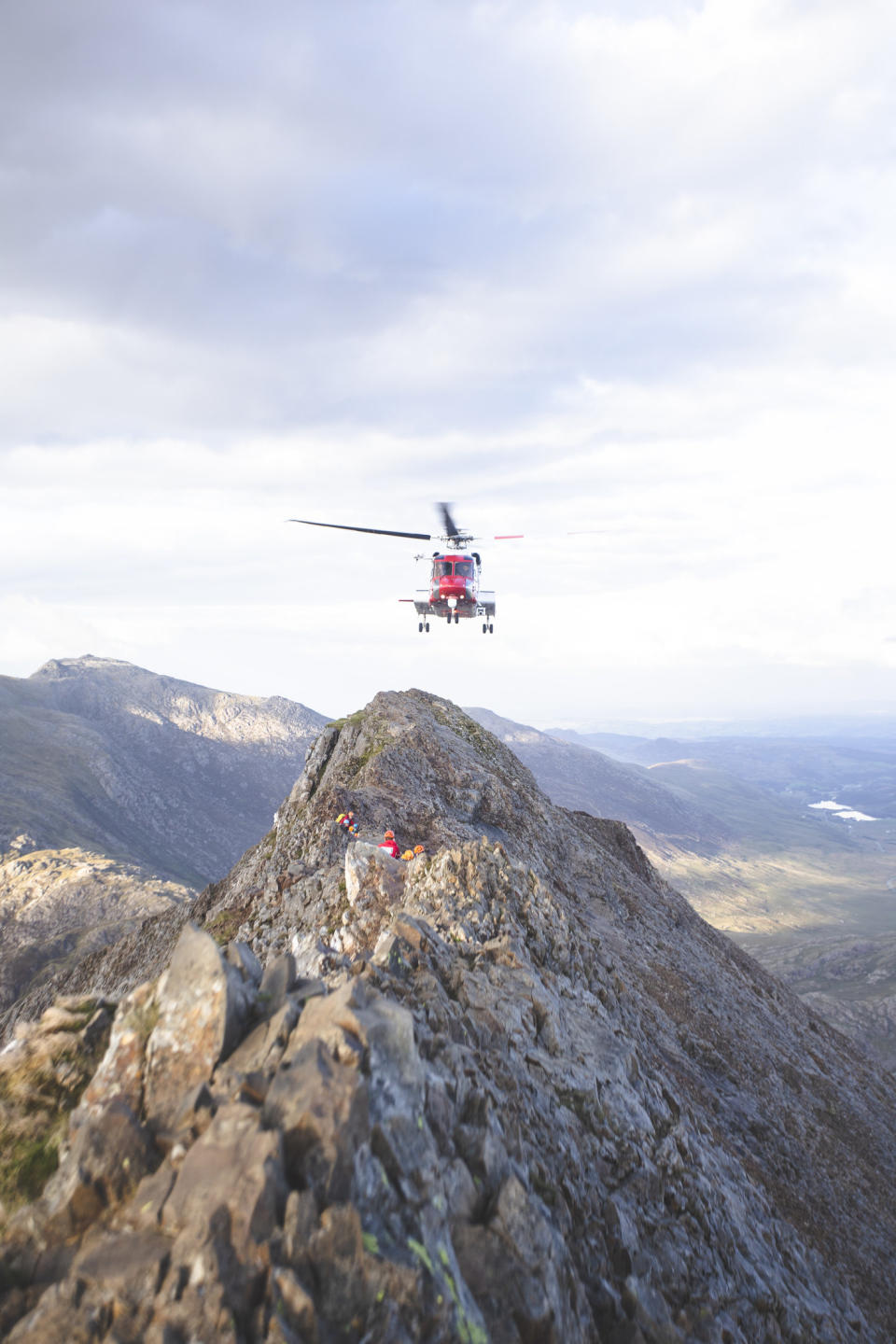 red helicopter pulling up over a mountain and hikers