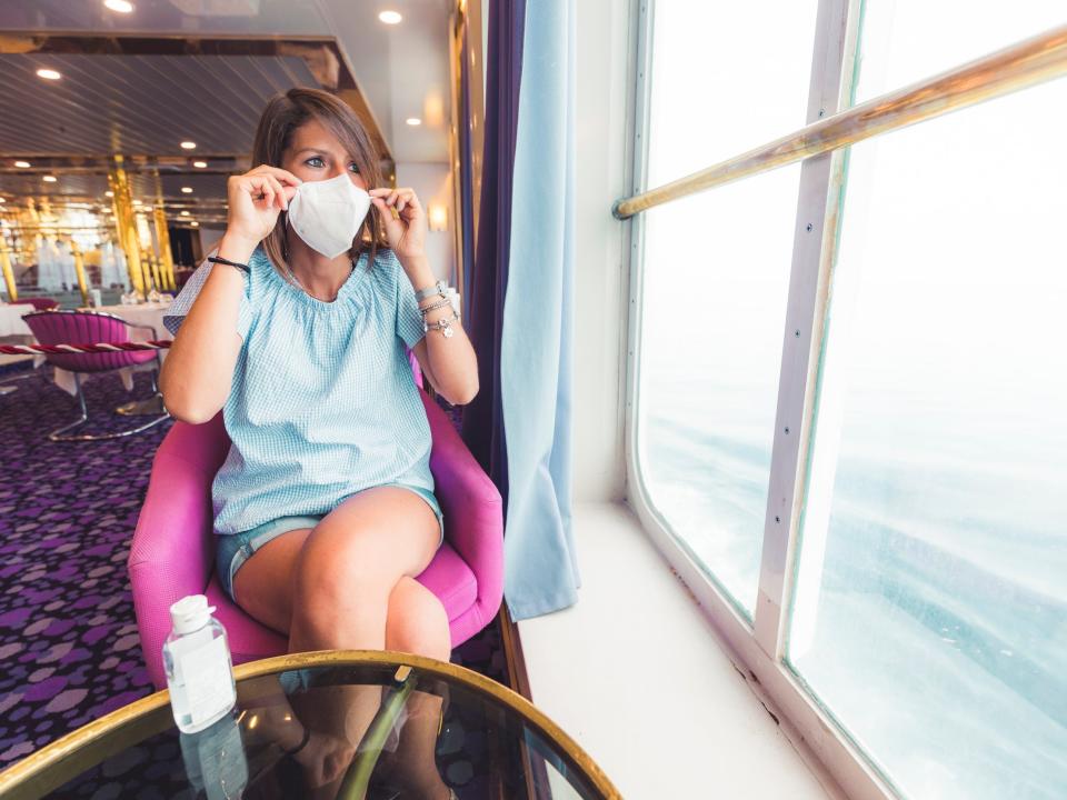 A person wearing a face mask while staring out a window on a cruise ship in Italy.